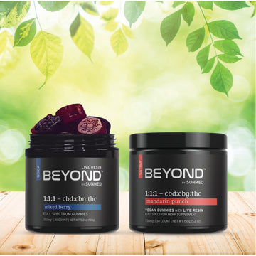 The Sunmed CBD BEYOND Sativa + Indica Gummies Bundle features mixed berry and mandarin punch flavors, shown on a wooden surface with a leafy background. Enjoy both delicious varieties in one convenient pack.