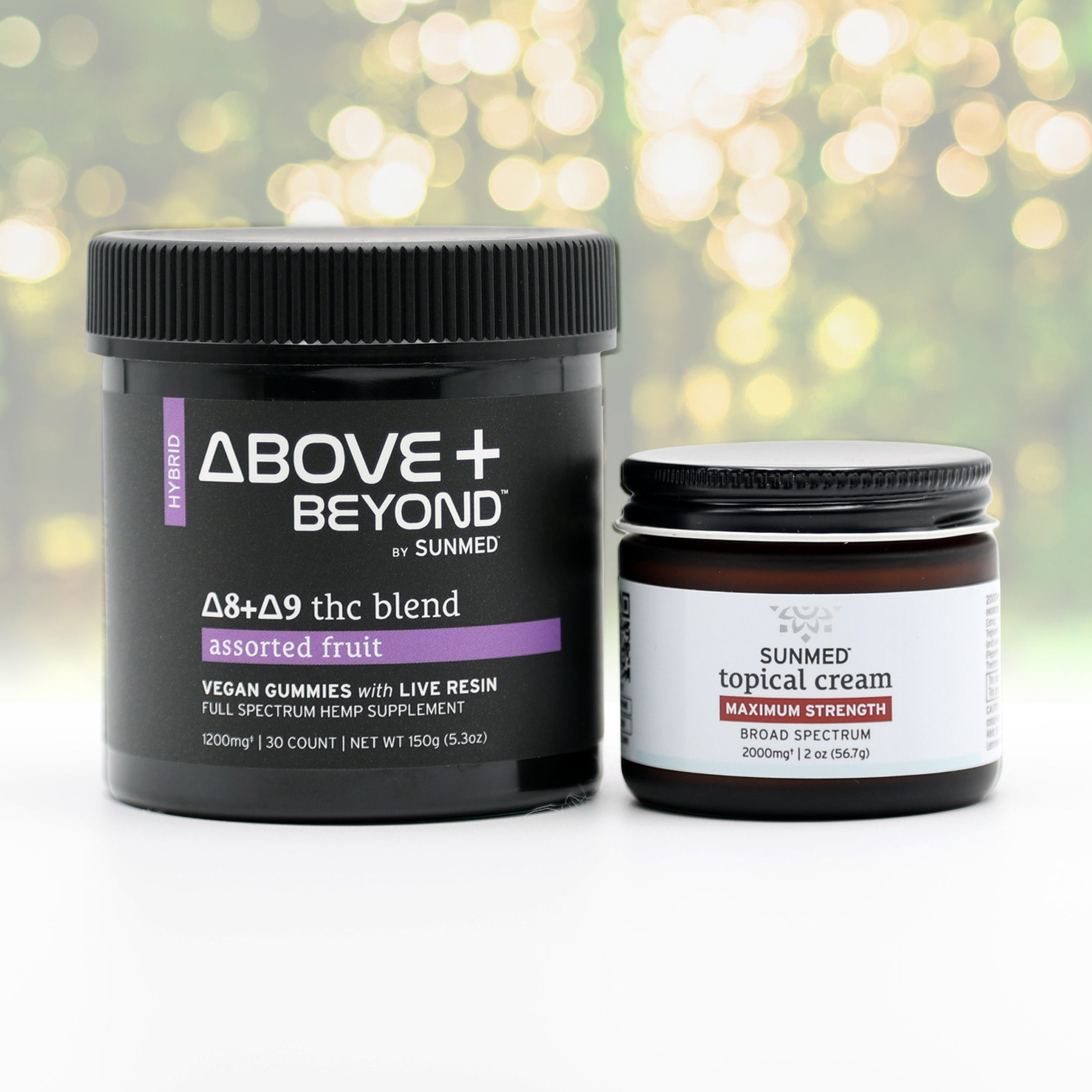 Two black jars from Sunmed CBD’s ABOVE + BEYOND Gummies + Topical Cream Bundle rest on a white surface, offering a soothing duo with nature-inspired relief, set against blurred greenery.