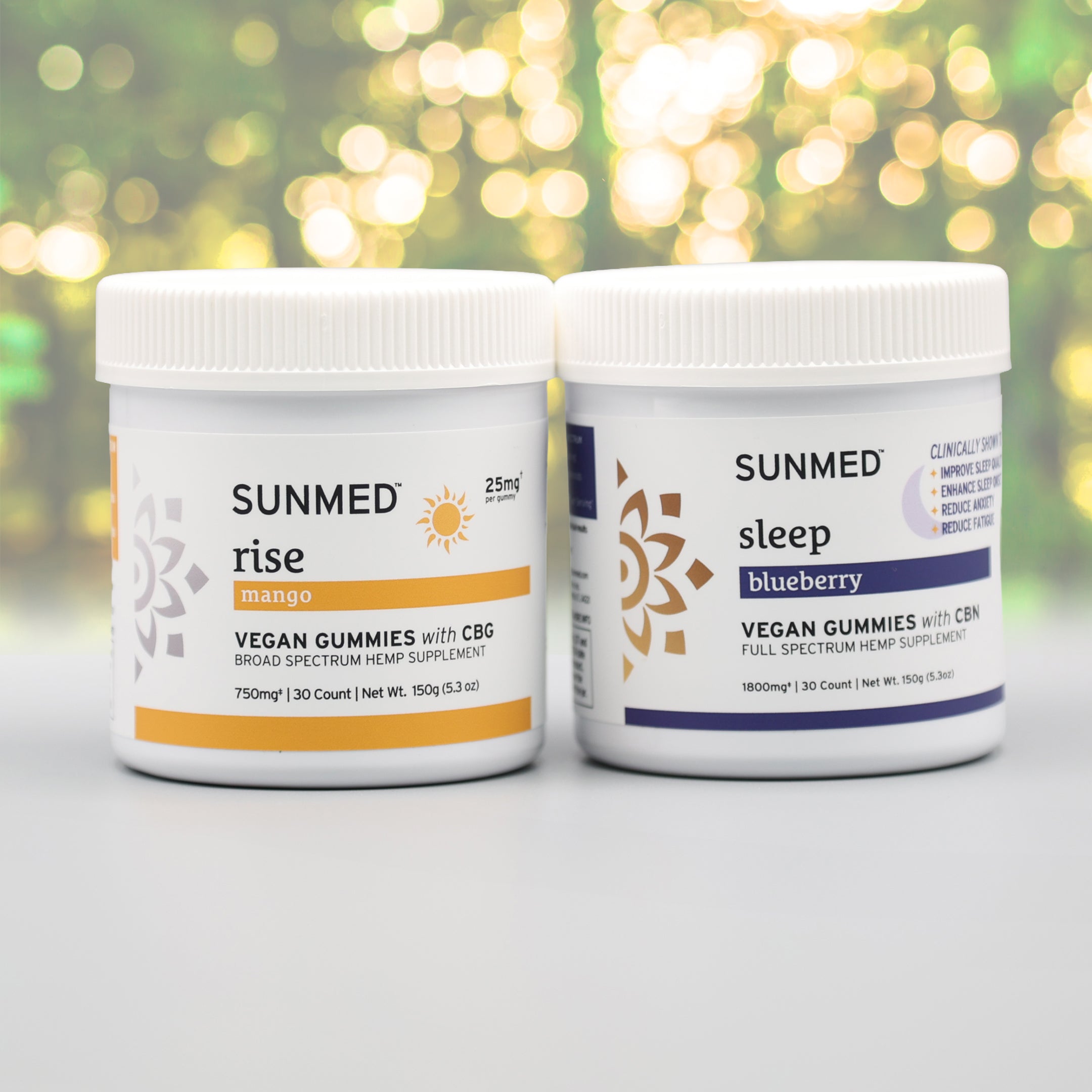 Two Sunmed CBD Full Spectrum Sleep + Rise Gummies containers—one mango (“rise”) and one blueberry (“sleep”)—sit on a gray surface, offering gummies for a morning boost or restful sleep in one convenient bundle.