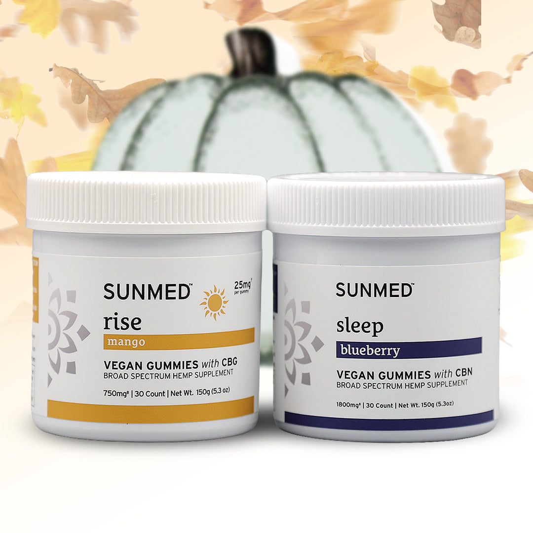 The Sunmed CBD Broad Spectrum Sleep + Rise Gummies Bundle features two jars—one mango-flavored for rise and one blueberry-flavored for sleep—with a white pumpkin in the background, making it an ideal THC-free wellness choice packed with delicious CBN and CBG gummies.