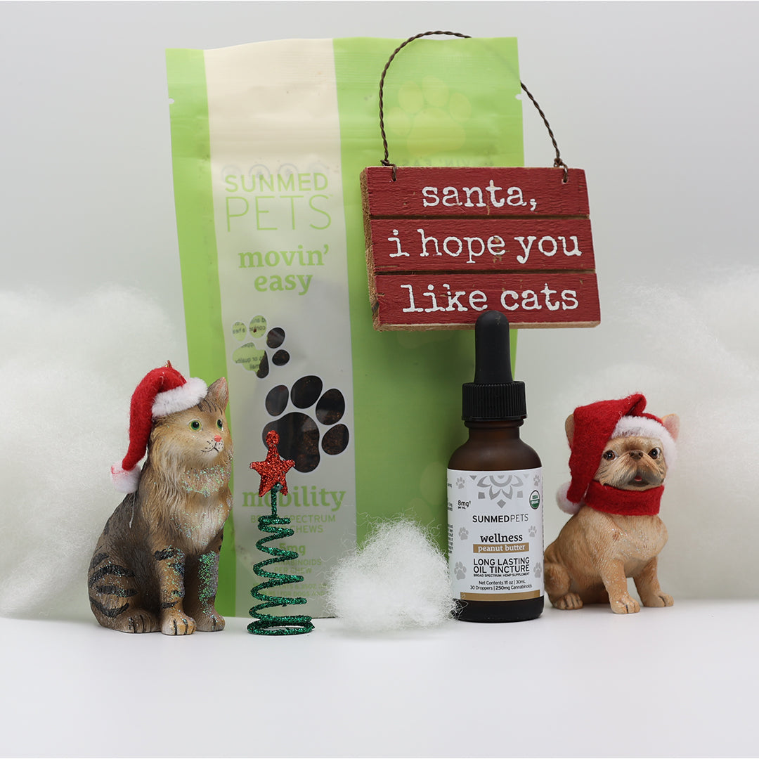 The Sunmed CBD Movin' Easy Pet Chews + Pet Tincture Bundle, plus two toy pets with Santa hats, cat treats, and a "santa, i hope you like cats." sign—perfect for pet wellness and joint health this holiday season.