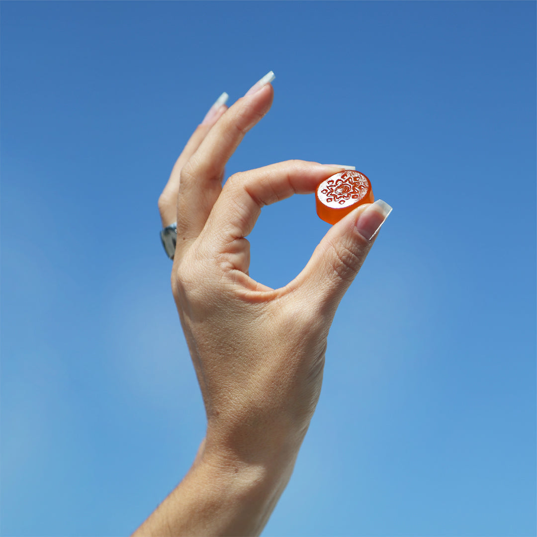 A hand holding a small, red circular object, like Sunmed CBD's Beyond 1:1:1 Sativa Live Resin Gummies, against a clear blue sky background.