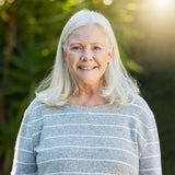 Smiling older woman with gray hair and striped sweater stands outdoors in sunlight, looking well-rested after using Sunmed CBD’s Full Spectrum Sleep CBN Gummies to improve her sleep quality.