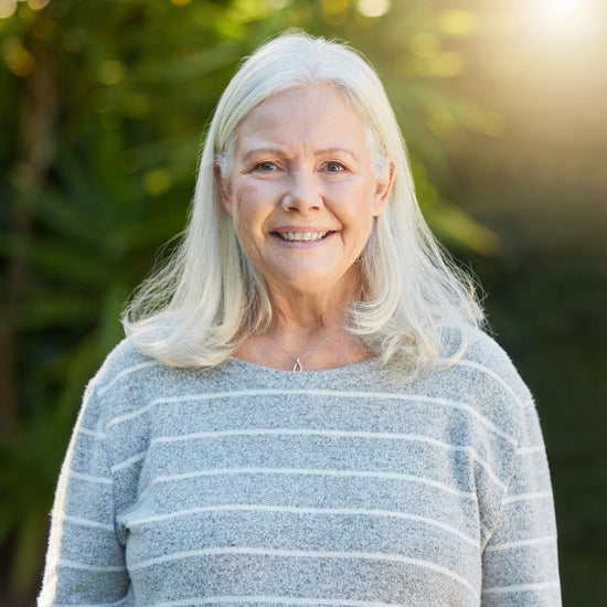 Smiling older woman with gray hair and striped sweater stands outdoors in sunlight, looking well-rested after using Sunmed CBD’s Full Spectrum Sleep CBN Gummies to improve her sleep quality.