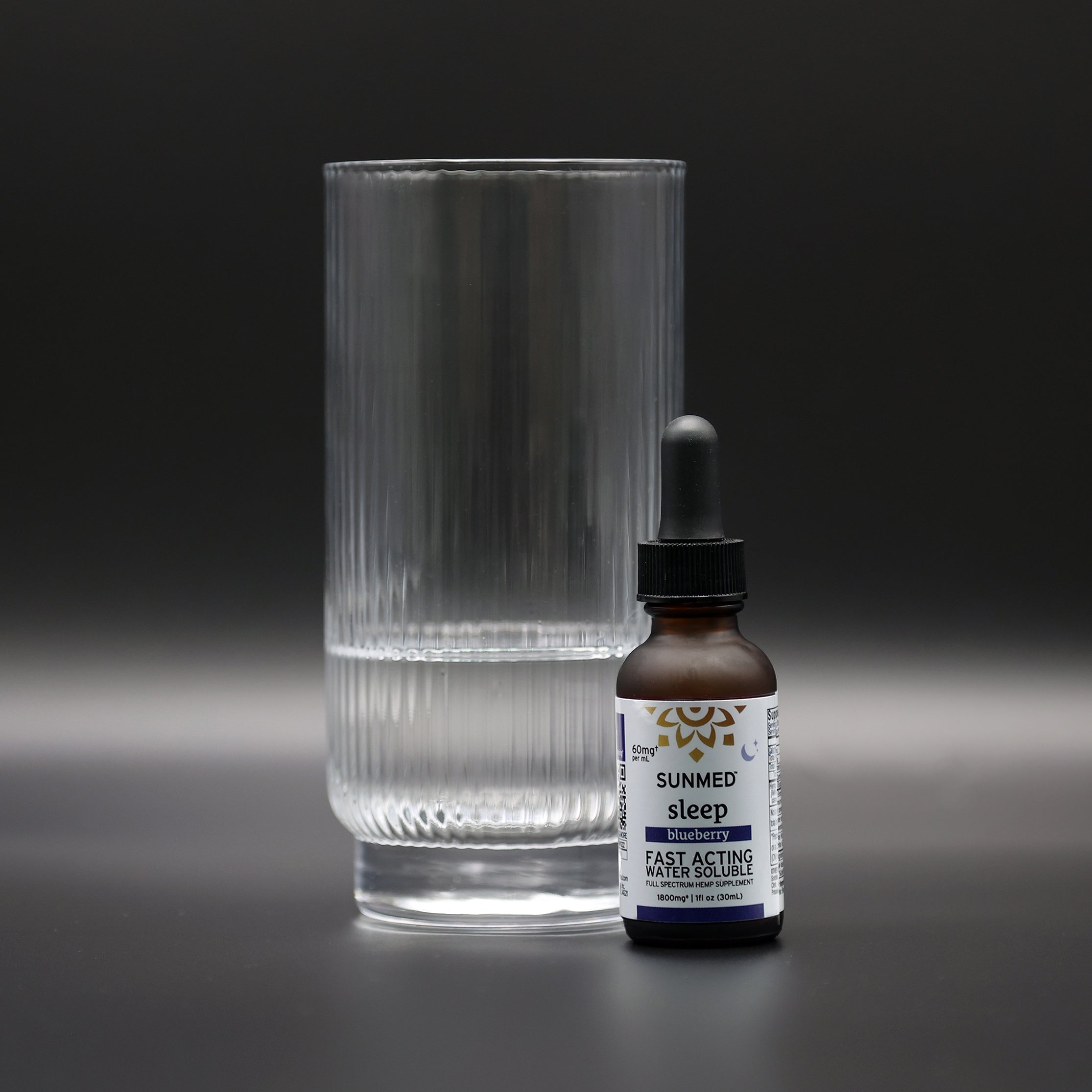A glass of water sits beside a Sunmed CBD Full Spectrum Sleep CBN Water Soluble dropper bottle, set against a dark background.