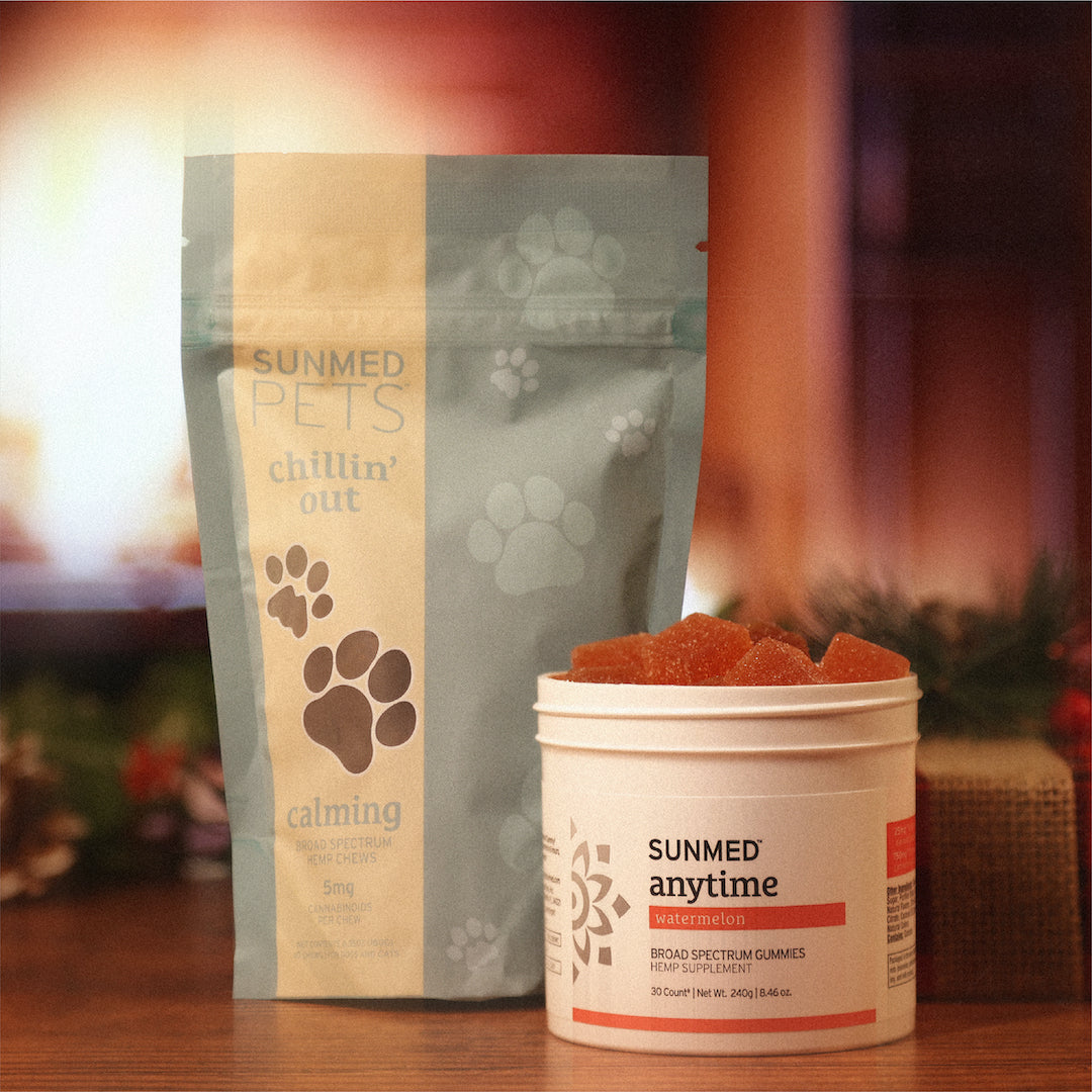 A table with holiday decor in the background featuring the Anytime Gummies + Chillin' Out Pet Chews Holiday Bundle from Sunmed CBD.