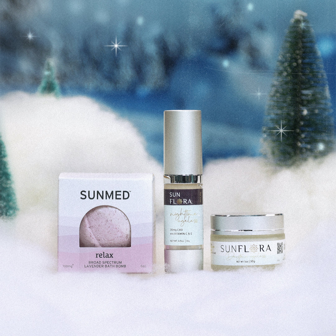 Sunmed CBD's Daytime + Nighttime Cream + Bath Bomb Holiday Bundle is beautifully showcased on snow, framed by two small evergreen trees, creating a peaceful ambiance. This serene setting highlights the soothing bath bombs and timeless moisturizers, providing an ideal fusion of natural beauty and skincare for your relaxing moments.