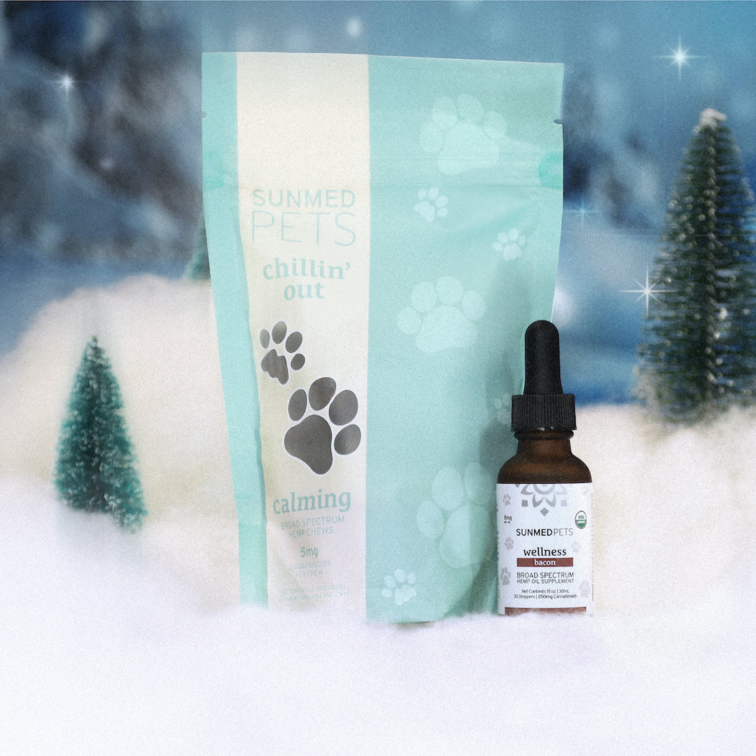 The Chillin' Out Pet Chews + Pet Tincture Holiday Bundle by Sunmed CBD in a snowy holiday scene with pine trees.