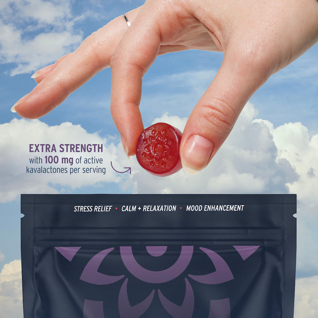 A hand holds a calming Kava Gummy from Sunmed CBD above a sleek black package, set against a backdrop of sky and clouds.