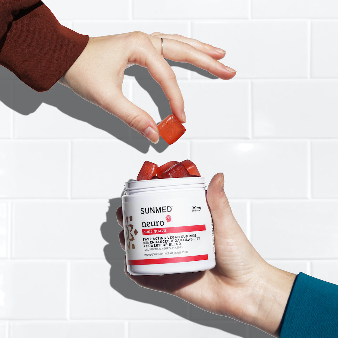 Two hands holding and taking red Full Spectrum Neuro Water Soluble CBD Gummies from a jar with a white tiled background. The label reads "Sunmed CBD," highlighting their fast-acting focus and enhanced bioavailability properties.