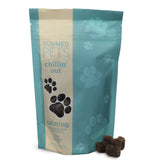 A light blue Sunmed CBD Broad Spectrum Chillin’ Out CBD Pet Chews bag for dogs, decorated with paw prints, sits beside some tasty hemp chews.