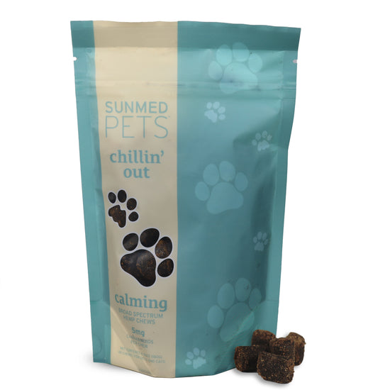 A light blue Sunmed CBD Broad Spectrum Chillin’ Out CBD Pet Chews bag for dogs, decorated with paw prints, sits beside some tasty hemp chews.