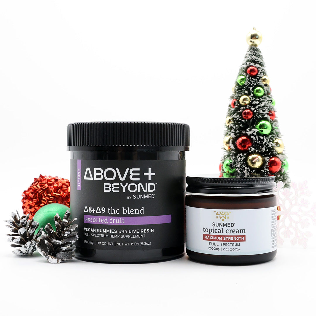 Two Sunmed CBD ABOVE + BEYOND Gummies + Topical Cream Bundle products are displayed with a decorated Christmas tree and festive ornaments in the background.