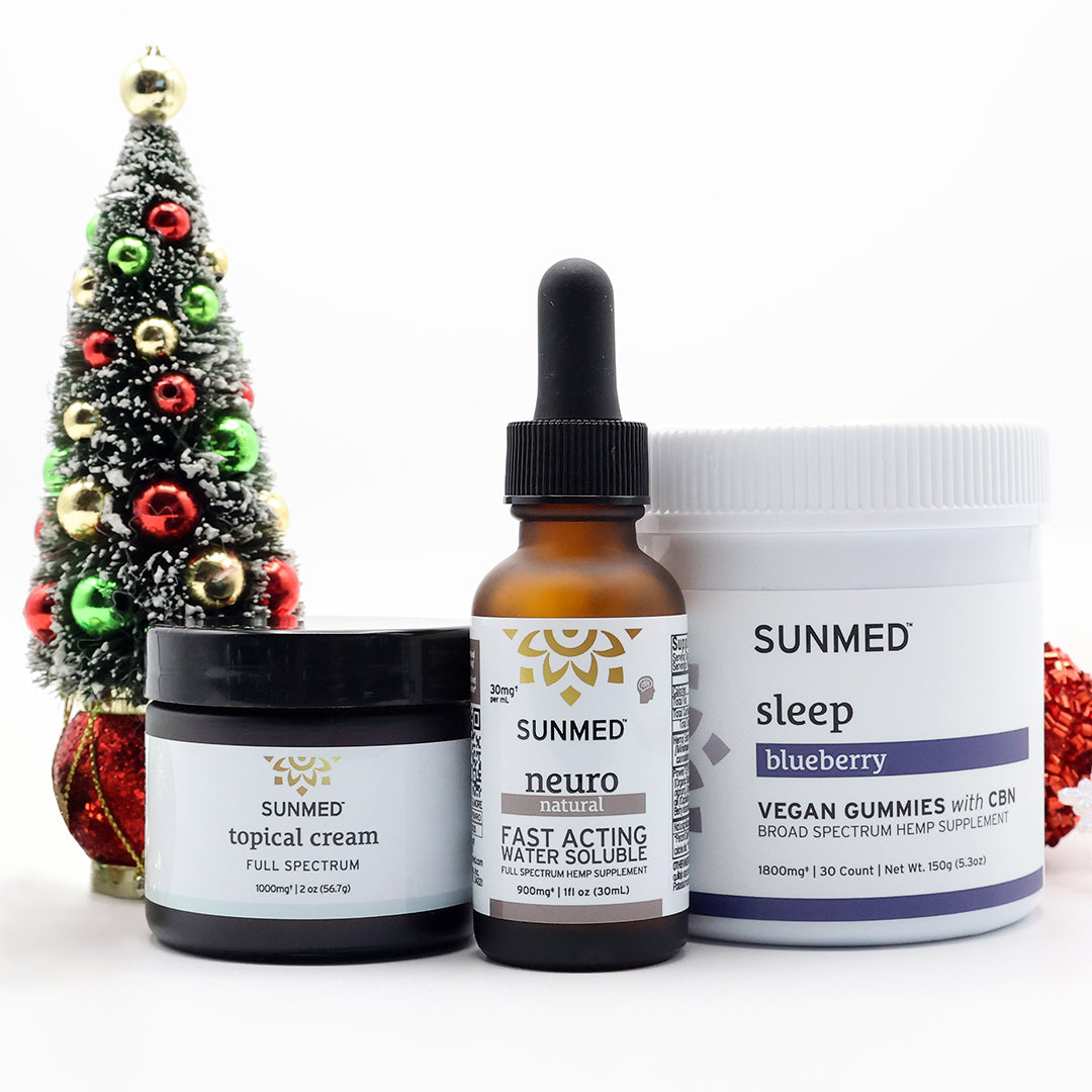 Three Sunmed CBD products—a Broad Spectrum Sleep Gummies + Neuro Water Soluble + Topical Cream Bundle—are displayed next to a small decorated Christmas tree on a white background.